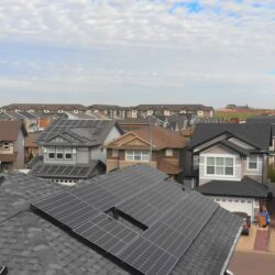 A suburban neighborhood with multiple houses featuring rooftop solar panels under a partly cloudy sky, showcasing the adoption of residential solar energy solutions.